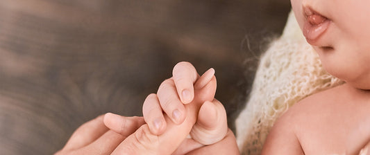 A close-up image of a baby's tiny hand gently grasping an adult's finger, highlighting the instinctual reflexes present from birth.