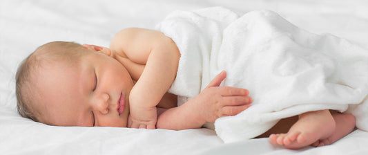 A peaceful newborn sleeps soundly, wrapped in a soft white blanket on a comfortable bed, showcasing the serene and restful state of an infant.