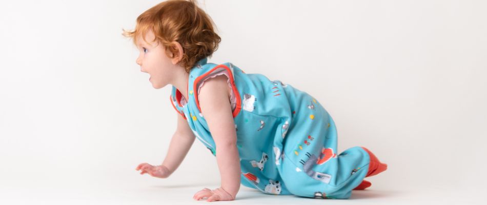 A crawling toddler in a blue sleeping bag with feet with a playful animal print.