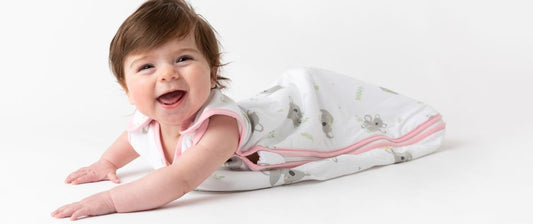  A joyful baby on her stomach flashes a wide smile, dressed in a sleep sack with a cute koala print, conveying a moment of pure happiness and delight.