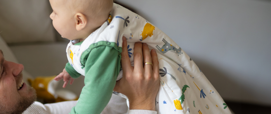 dad holding up a baby wearing a green and white baby sleeping bag