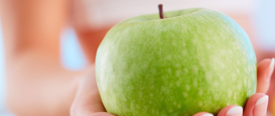 A close-up of a hand holding a vibrant green apple, symbolizing healthy eating and its benefits for fertility.
