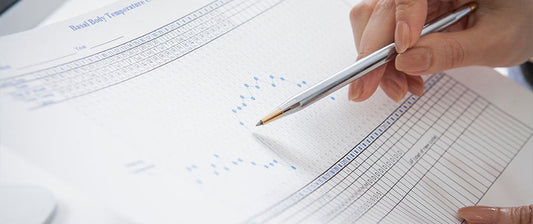 A person marks data on a basal body temperature chart, used for tracking fertility cycles.