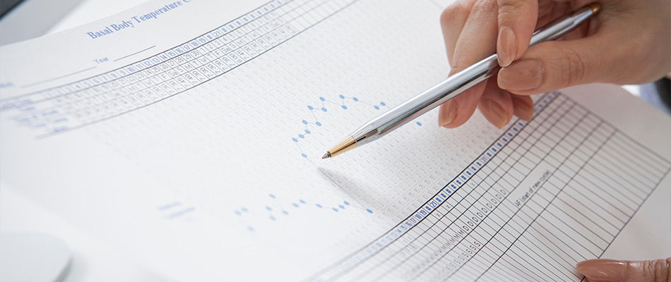 A person marks data on a basal body temperature chart, used for tracking fertility cycles.