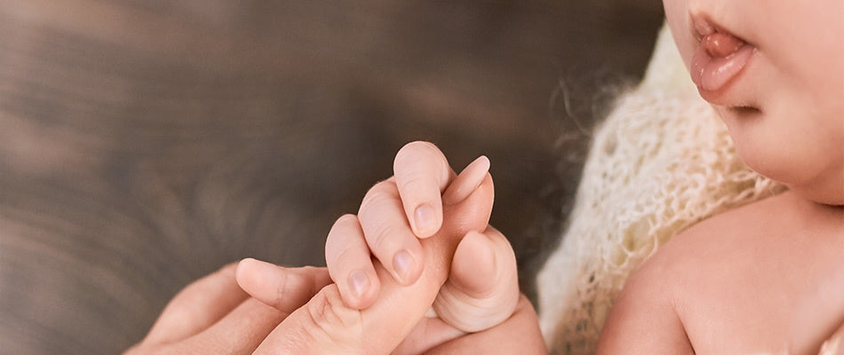  A close-up image of a baby's tiny hand gently grasping an adult's finger, highlighting the instinctual reflexes present from birth.