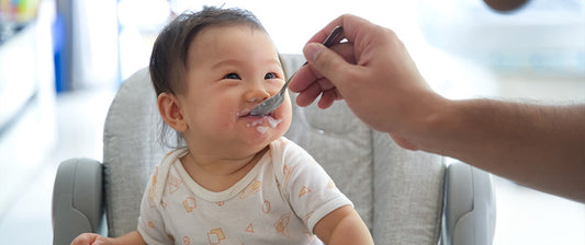  A happy toddler enjoys being fed by an adult, food smeared playfully on their face, capturing a joyful mealtime moment.