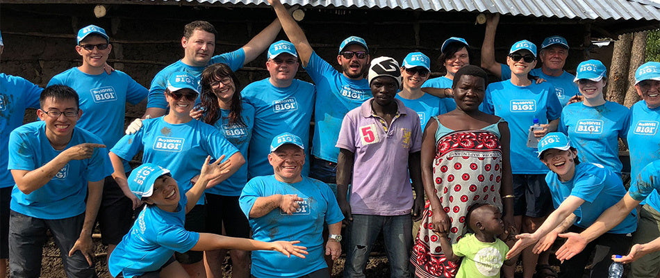  A group of volunteers in matching blue shirts pose happily with local residents in a rural setting, demonstrating a moment of community and collaboration during a service trip.