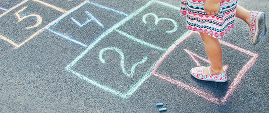 A child plays hopscotch on a chalk-drawn court, demonstrating a classic outdoor game that combines physical activity with simple counting skills.