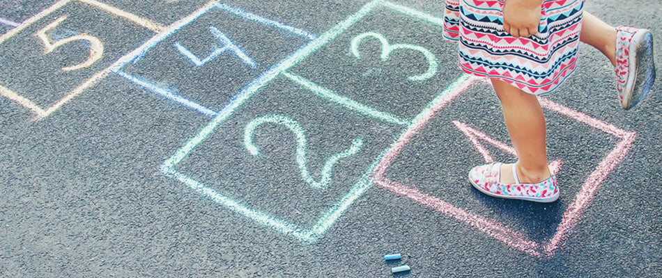 A child plays hopscotch on a chalk-drawn court, demonstrating a classic outdoor game that combines physical activity with simple counting skills.