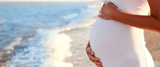 a pregnant woman standing by the sea, gently cradling her belly