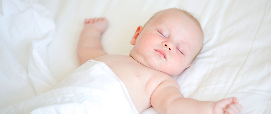 A baby sleeps peacefully on a white duvet, arms gently outstretched.