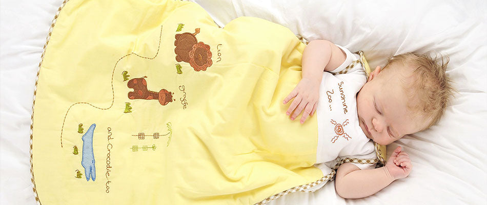 A baby sleeps under a yellow blanket embroidered with animal motifs, exuding peacefulness.